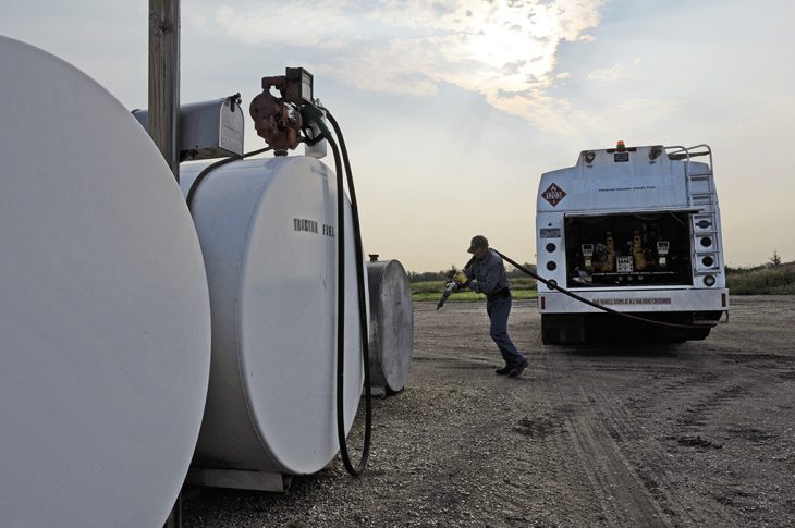 Man pulling a hose from a propane truck to a tank for a refill